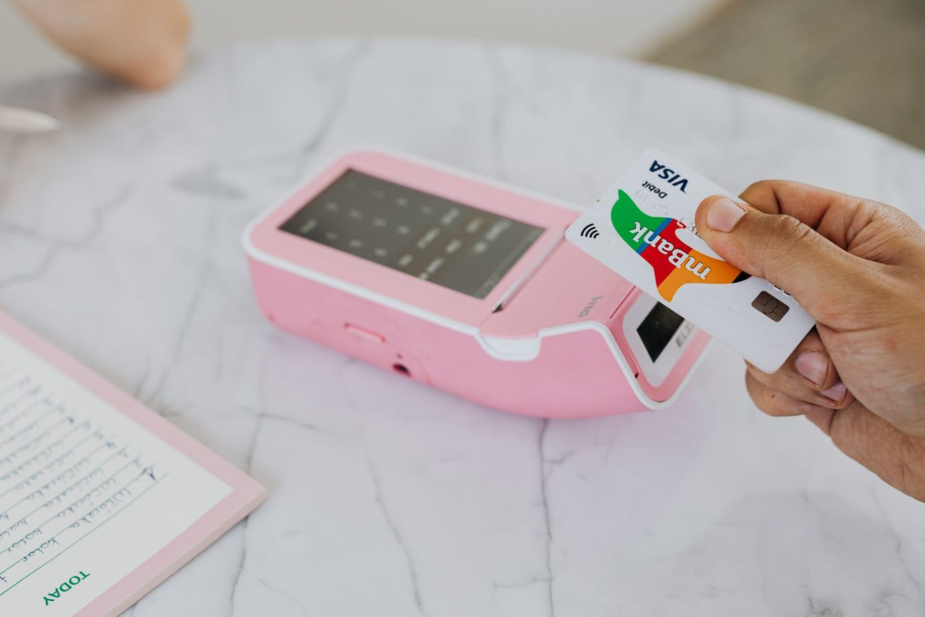 A customer tapping a bank card on a payment terminal at a shop counter