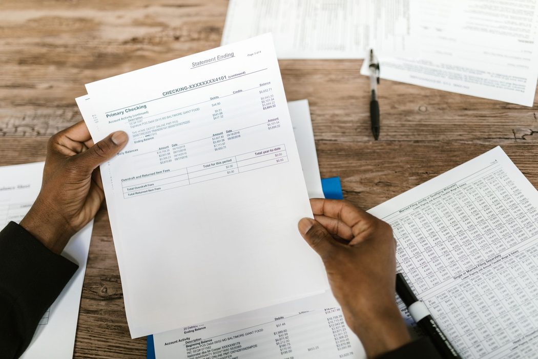 A person reviewing a printed bank statement at a desk, checking transaction details