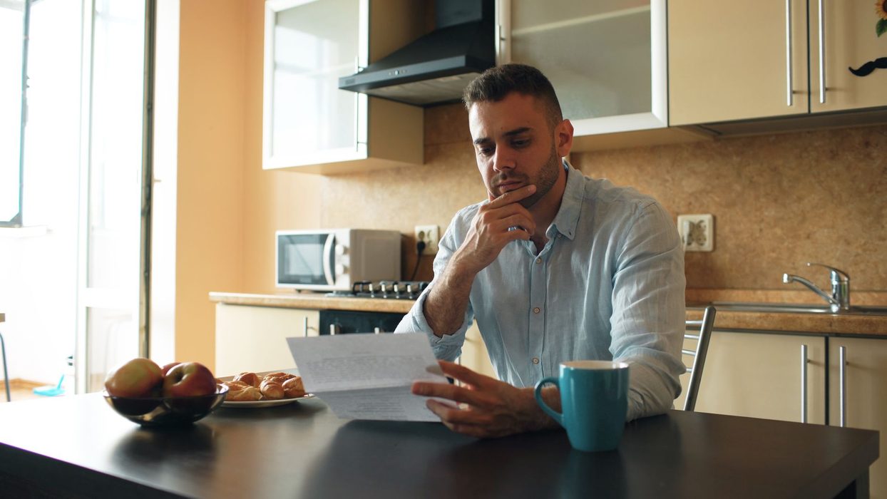 A person at a kitchen table comparing a printed bank statement with a phone screen