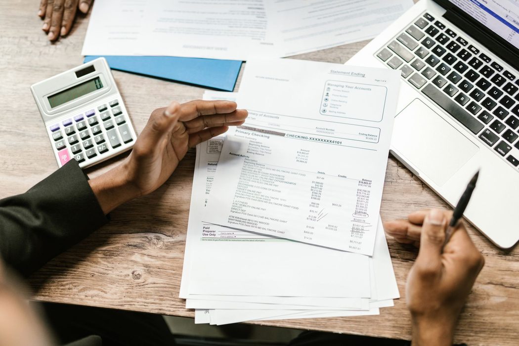A person comparing a printed bank statement with account activity on a laptop screen